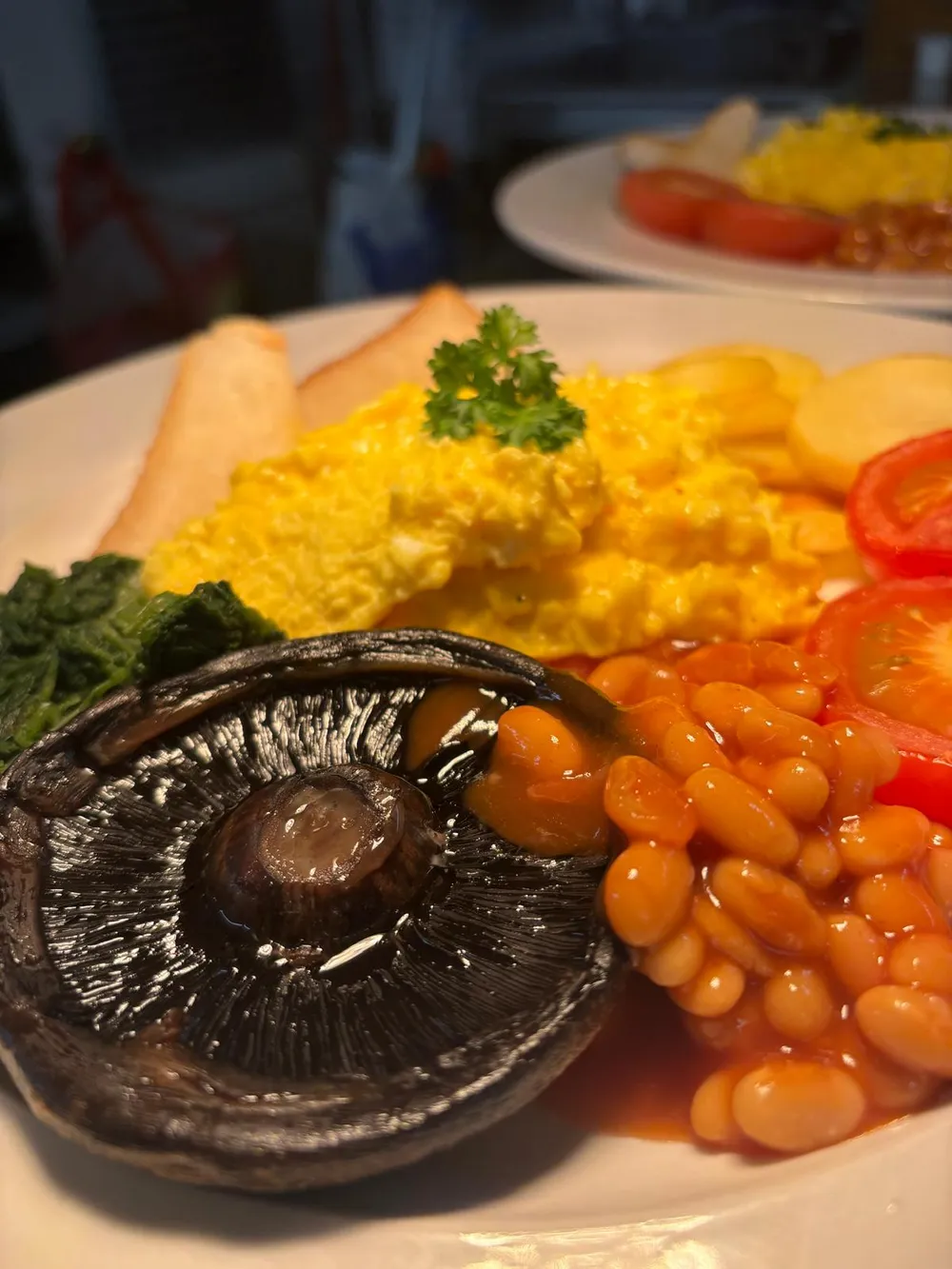 A freshly cooked breakfast with scrambled eggs, mushroom, beans and tomato